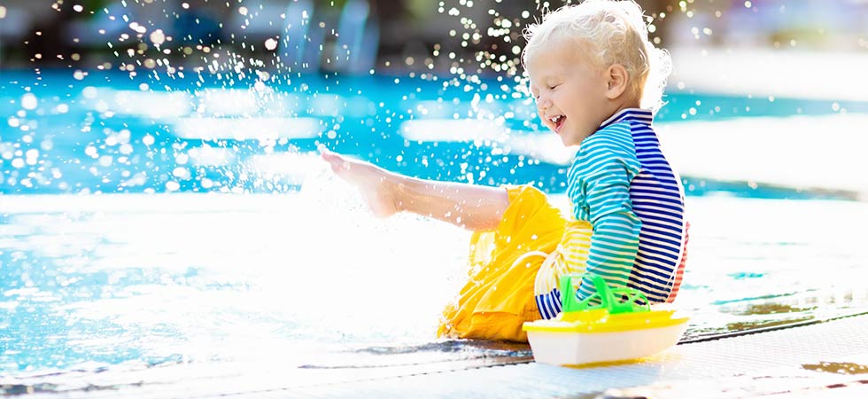 Young child smiling and kicking his feet in the water of a pool