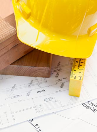 Yellow hard had, piece of lumber, and a ruler sitting on top of architectural plans